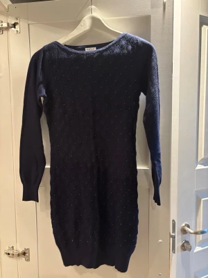 Mörkblå stickad tröja från Kaylla - Snygg mörkblå stickad tröja från Kaylla Paris med långärmad design och diskret mönster framtill. Tröjan har en rund hals och är figurnära i passformen, perfekt för dig som gillar stilrena och klassiska plagg med lite extra struktur.