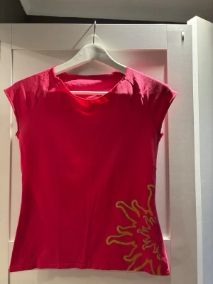 Rosa Puma t-shirt med tryck - Säljer en rosa t-shirt från Puma med korta ärmar och coolt gult tryck nertill. Puma-loggan är broderad i gult på ärmen. T-shirten har en avslappnad passform och är gjord i mjuk bomull, perfekt för dig som gillar sportiga vibes.