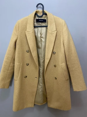 Beige kappa från Zara Basic - Säljer en snygg beige kappa från Zara Basic med dubbelknäppning och klassisk krage. Jackan har två fickor framtill och är helfodrad. Perfekt för dig som vill ha en stilren och tidlös look till höst och vinter.