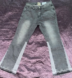 Grå bootcut jeans från Gallery Dept. - Säljer ett par grå jeans från Gallery Dept. med bootcut-snitt och coola ljusare paneler längs benen. Klassisk femficksdesign och tydliga sömmar. Jeansen har en schysst tvättad look och är tillverkade i jeansmaterial. Perfekt för dig som gillar streetwear och unik stil.