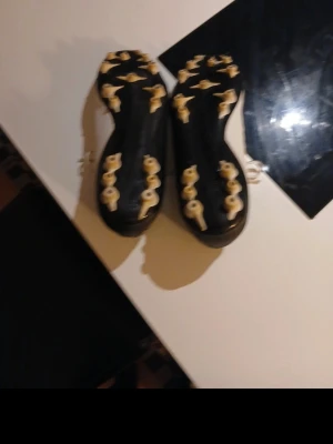 Nike Phantom GX fotbollsskor vit/svart/guld - Säljer ett par Nike Phantom GX fotbollsskor med snygg design i vitt, svart och guld. Skorna har snörning och rund tå, samt platt sula med fasta dobbar för bra grepp på planen. Materialet är syntet och skon har en cool guldlogga på sidan.