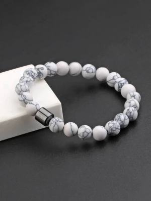 Ingen väst på bilderna - Bilderna visar ett armband med vita och gråmelerade pärlor, samt en svart cylinderformad detalj.