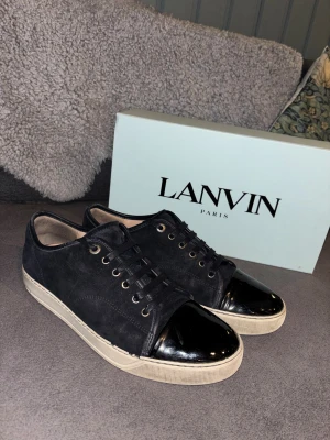 Lanvin svarta sneakers med lackad tå ”MED KVITTO” - Lanvin sneakers i svart mocka med vit sula och glänsande svart lackad tå. De enda defekterna är vid omsyeningen har det lossnat lite, vilket gör att tråden syns vid två olika ställen (Lite otydlipå bildrna, fråga för fler bilder). Annars suveränt skick och allt på bilder följs med inklusive KVITTO!! Storlek uk 9 passar typ 43-44. Om frågor är det bara att ställa så svara jag så snabbt jag kan😀. Säljs för ett sjukt pris —> nypris 5200, mitt pris 2199!!😀🤝