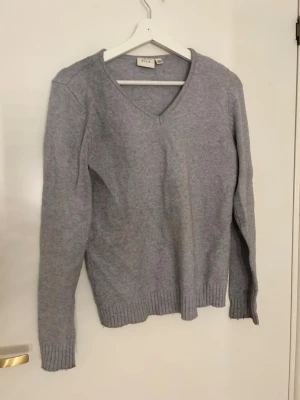 Grå stickad tröja från VILA - Mysig grå stickad tröja från VILA med v-ringad hals och ribbade muddar vid ärmslut och nederkant. Perfekt för lager-på-lager och chill dagar. Enkel design som funkar till jeans eller kjol.