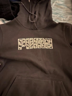Svart hoodie med vit text PUMA  - Fin svart hoodie med vit text PUMA perfekt för vinter när man ska åka skridskor eller skidor under en jacka. ( den är oversized så man kan ha på sig den vid 165 ungefär )