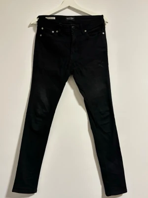 Svarta Jack & Jones - Svarta skinny fit jeans från Jack & Jones, modell Liam. Byxorna har fem fickor, dragkedja och knapp framtill samt detaljerade sömmar vid knäna. Materialet är jeans med stretch för extra komfort. Passar dig som gillar en tajt och modern look.