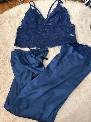 Mörkblå spetsett tröja+byxor med omlottband - Säljer en mörkblå sett  med v-ringad hals och tunna axelband. Setter är gjord i spets med b och har ett omlottband framtill. Perfekt för dig som gillar en feminin och trendig look. Materialet är mjukt och har en lyxig känsla.