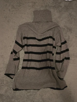 Randig polo - Mysig polo i beige/grå med svarta horisontella ränder. Tröjan är stickad, har lång ärm och en hög polokrage. Passformen är loose och modellen är lite längre, perfekt till jeans eller leggings. Aldrig använd, därav priset. Säljer då den inte används.