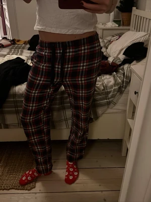 Röd-rutiga mjukisbyxor med snörning - Säljer ett par sköna mjukisbyxor med röd, vit och svart rutigt mönster. Byxorna har snörning i midjan och en bakficka med rutigt tyg. Perfekta för chill hemma och har en loose passform.