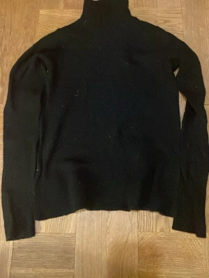 Svart polotröja i merinoull - Klassisk svart polotröja från Cubus i 100% mjuk merinoull. Tröjan har lång ärm och hög polokrage, perfekt för lager på lager under kyliga dagar. Enkel och stilren design som funkar till allt. Står inte storlek men är för liten för S. Storlek XS. 