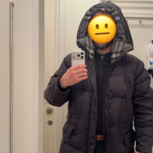 Burberry Hartson down parka - Storleken passar S/M Svart pufferjacka från Burberry med rutigt foder i huvan. Jackan har dragkedja och knappar framtill, samt två fickor med lock. Materialet är polyamid, ull och kashmir. Perfekt för kalla dagar och har en schysst oversized look. 