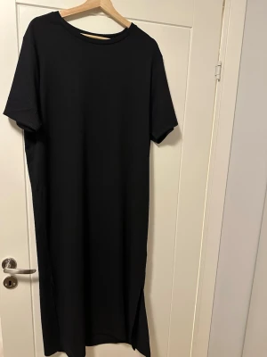 Svart långklänning från Lager 157 - Svart långklänning från Lager 157, modell Selma. Klänningen har rund halsringning, korta ärmar och slits på sidorna. Enkel och stilren design i mjukt material som känns skönt mot huden. Perfekt för dig som gillar minimalistisk stil. Aldrig använd, dock tvättad en gång :)