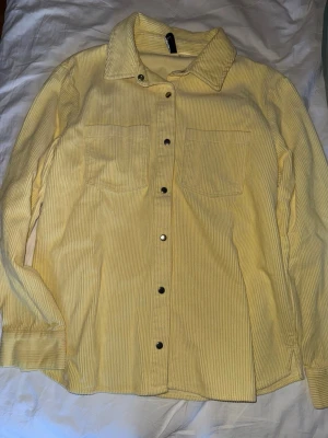 Gul skjorta  - Säljer en ljusgul overshirt i manchester från H&M. Skjortan har långa ärmar, två bröstfickor och tryckknappar framtill. Perfekt för lager på lager och ger en chill vibe till din outfit.
