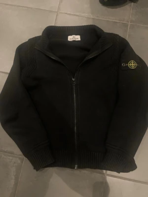stickad Stone Island kofta - Säljer en fräsch svart stickad kofta från Stone Island i storlek 12 år och passar mellan 156-166. Passar perfekt för kyliga dagar med enkel och stilren design som funkar till det mesta. (Pris går att diskutera!)