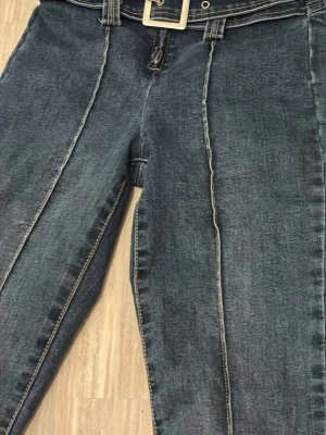 Blå bootcut jeans med bälte - Snygga blå bootcut jeans med markerad söm längs benen och medföljande bälte med fyrkantigt spänne. Jeansen har klassisk denimlook och är tillverkade i jeansmaterial. Perfekt för dig som gillar retrovibbar och vill sticka ut med coola detaljer.