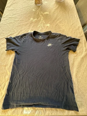 Svart Nike t-shirt i bomull XL - Svart t-shirt från Nike i storlek XL, med klassisk rund hals och korta ärmar. Materialet är mjuk bomull och på bröstet finns en broderad Nike-logga i vitt. Perfekt för dig som gillar sportiga och stilrena plagg.