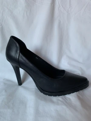 Svarta pumps från Reschia - Säljer ett par stilrena svarta pumps från Reschia med spetsig tå och hög klack på 10 cm. Skorna är tillverkade i skinn och har en klassisk, elegant form men med en lite grövre sula vilket ger dem ett coolare uttryck än vanliga pumps. Använda någon enstaka gång så i mycket gott skick. 