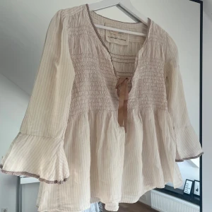 Odd Molly blus med broderad fjäril - Supersöt ljusrosa blus med diskreta ränder och volangärmar. Storlek , motsvarar S. V-ringad med rosett i satinband och broderad fjäril på ena ärmen. Tunt, luftigt material som känns perfekt för vår och sommar.