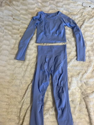 Blå träningstights och topp från SOC - Säljer ett set med ljusblå träningstights och matchande långärmad topp från SOC. Båda plaggen har ribbade detaljer och loggan är invävd i midjan. Materialet är stretchigt och syntetiskt, perfekt för träning och rörelse.