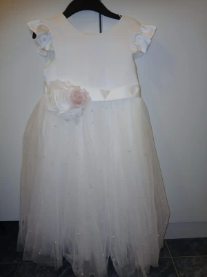 Vit långklänning med blommor och pärlor - Superfin vit långklänning med fluffiga korta ärmar och ett skirt tylllager dekorerat med små pärlor. Midjan pryds av två stora tygblommor i vitt och ljusrosa. Klänningen har en elegant och romantisk look, perfekt för speciella tillfällen.