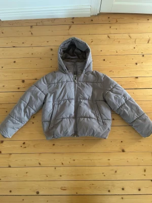 Grå pufferjacka från Nelly med huva - Säljer en grå pufferjacka från Nelly i storlek 36. Jackan har en skön huva, dragkedja framtill och två sidofickor. Perfekt för kyliga dagar🩵