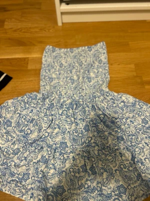 Blåvit smockad tubtopp från Sister - Säljer en blåvit tubtopp från newyorker i storlek M. Toppen har ett smockat liv och ett vackert paisleyinspirerat mönster i blått på vit botten. Perfekt för varma dagar och enkel att styla med jeans eller kjol.