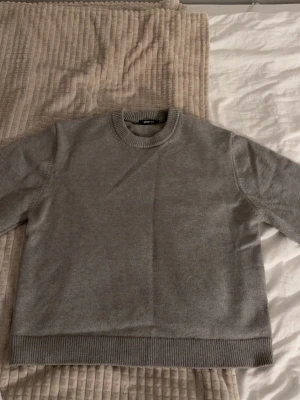 Grå stickad tröja från Gina Tricot - Säljer en enkel och snygg grå stickad tröja från Gina Tricot. Tröjan har rund hals, ribbade muddar vid ärmslut och nederkant samt långärmad passform. 