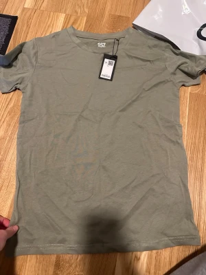 Grön t-shirt från 157 i bomull - Snygg grön t-shirt från 157 i storlek XS. Modellen är klassisk med rund hals och korta ärmar. Tillverkad i 100% mjuk bomull som känns skön mot huden. Perfekt för dig som gillar enkel och clean stil.