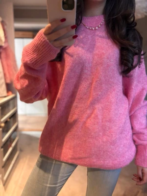 Rosa stickad tröja mohair - Mysig rosa mohair stickad tröja med rund hals och ribbade muddar. Modellen är loose fit och har långa ärmar, perfekt för att hålla sig varm under kyliga dagar. Passar snyggt till jeans och har en mjuk, fluffig känsla. 