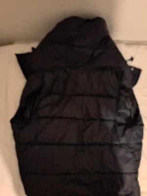 Svart pufferjacka från Burberry M - Svart pufferjacka från Burberry i storlek M. Jackan har klassiskt rutigt Burberry-foder, huva och quiltad design. Materialet är polyester och bomull, vilket gör den både lätt och varm. Perfekt för kalla dagar och har en snygg, tidlös look.