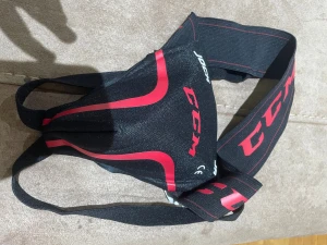 Svart och rött hockey suspensoar-bälte CCM - Säljer ett svart suspensoar-bälte från CCM med röda detaljer och logga. Bältet har bred resår och är designat för att ge skydd vid hockey eller annan sport. Materialet är slitstarkt syntet och passformen är justerbar med elastiska band.