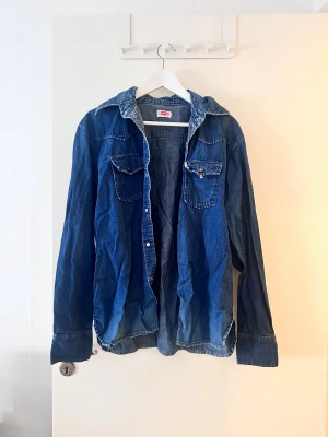 Blå jeansskjorta från Levi's - Snygg blå jeansskjorta från Levi's med klassisk krage och två bröstfickor med knappar. Skjortan har lång ärm och är tillverkad i bomull. Perfekt för en avslappnad och cool look.