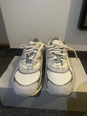 Skor - Säljer ett par snygga Asics sneakers i vitt och grått med mesh- och mockadetaljer. Skorna har rund tå, platt sula och klassisk snörning. Perfekta för dig som gillar sportig stil och vill ha bekväma skor med cool design.