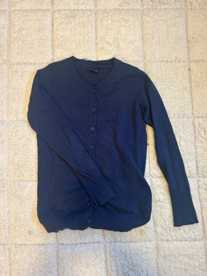 Mörkblå kofta - En klassisk mörkblå kofta från Cubus i storlek XS. Tröjan har långa ärmar, rund halsringning och stängs med fem matchande knappar framtill. Materialet är mjukt och tunt, perfekt för lager på lager under höst och vår.