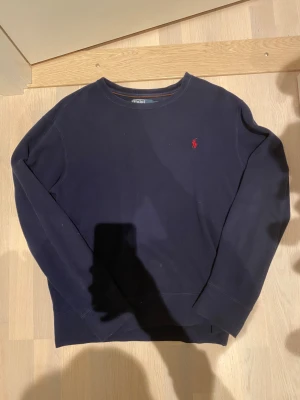 Mörkblå tröja från Polo Ralph Lauren - Snygg mörkblå tröja från Polo Ralph Lauren med klassisk röd logobrodering på bröstet. Rund hals och långa ärmar, tillverkad i mjuk bomull. Perfekt för dig som gillar stilrena och tidlösa plagg med en sportig touch. Säljer den då den inte kommit till så mycket användning passar perfekt om man har storlek S också. Priset är inte hugget i sten tveka inte på att höra av er om ni har några frågor 