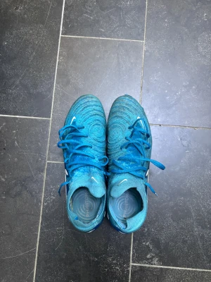 Nike Phantom Gx elite  - Säljer ett par Nike Phantom fotbollsskor i blått med silverfärgade swoosh-loggor. Skorna har snörning och en stickad ovandel med cirkulärt mönster. Sulan är utrustad med dobbar för gräsplan och insidan har Phantom-tryck. Perfekt för dig som vill ha snygga och funktionella skor på planen. Kan tänka mig gå ner i pris vid snabb affär 