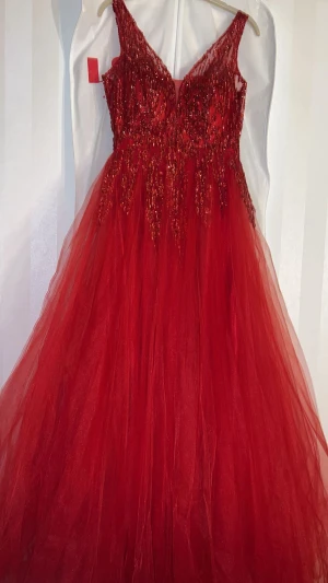 Röd balklänning  - Säljer denna magiska röda långklänningingen med glittriga paljetter på överdelen som är v-ringad. Kjolen är i flera lager tyll.Insidan är fodrad med satin för extra komfort. Perfekt för bal eller fest /bröllop och event. Den kom aldrig till användning så den är helt ny
