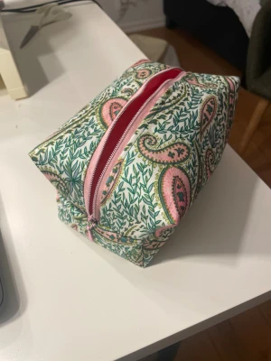  necessär  - Handsydd necessär i rosagrönt tyg. Bredd: ca18 cm, höjd: ca 9 cm. Finns även i ett svart, prickigt tyg