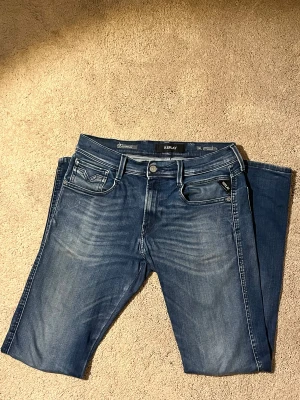 Replay Anbass jeans blå 30/32 - Snygga Replay Anbass jeans i klassisk blå tvätt med diskreta slitningar och kontrastsömmar. Modellen anbass hyperflex cloud, slim passform. Materialet är stretchigt jeans för extra komfort. Perfekta jeans för både vinter och kalla sommarkvällar. Nypris 1800kr mitt pris 600kr! Vid fler frågor bara skriv mvh Almen.