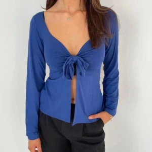 Blå Design by si topp - Snygg blå långärmad topp med knyt framtill och djup v-ringning. Perfekt för en stilren look. Använd fåtal gånger och i perfekt skick. Priset kan diskuteras vid smidig handel. 