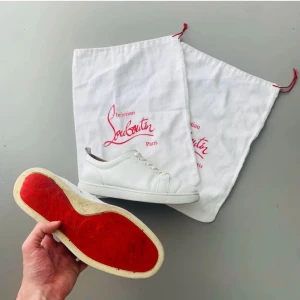 Vita sneakers från Christian Louboutin - Snygga vita sneakers från Christian Louboutin i skinn med klassisk röd sula. Modellen har rund tå, snörning och diskreta detaljer på sidan. Kommer med original dustbags. Perfekta för dig som vill ha en clean och lyxig look med en ikonisk touch.