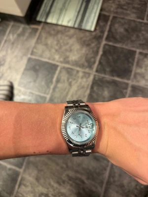 Seiko mod - Snygg klocka från Seiko med silverfärgat metallarmband och en ljusblå urtavla. Klockan har en rund boett med räfflad kant och den klassisk ” arabic dial l”. Länken är klassisk och har ett smidigt spänne. Perfekt för dig som gillar stilrena accessoarer.