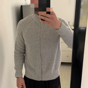 Grå ribbstickad kofta från Dobber - Säljer en grå ribbstickad kofta från Dobber i storlek M. Koftan har dragkedja framtill, hög krage och långa ärmar. Perfekt för lager-på-lager och chill dagar. Enkel och stilren design som funkar till det mesta.