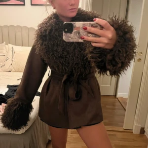 Brun pälsjacka från NA-KD med bälte - Säljer en brun pälsjacka från NA-KD med stora fluffiga detaljer vid krage och ärmslut. Jackan har bälte i midjan för snygg passform och är i en kortare modell. Perfekt plagg för höst och vinter 🩷slutsåld på hemsidan 