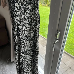 Svartvit långklänning med paisleymönster - Säljer en svartvit långklänning med tunna axelband och paisleyinspirerat mönster. Klänningen har en flowy siluett och är tillverkad i ett lätt material som ger en skön känsla. Perfekt för dig som gillar boho-vibe och vill sticka ut med ett coolt mönster. Passar även mindre storlekar då den är liten i storlek. 