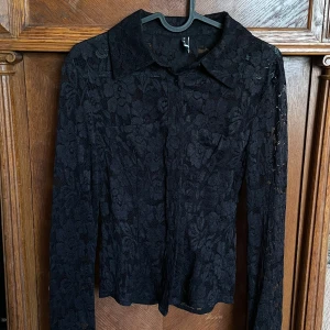 Svart spetsblus/skjorta - Supersnygg svart spetsblus från Gina Tricot med blommigt mönster. Skjortan har lång ärm, klassisk krage och knäppning framtill. Perfekt för dig som vill ha en feminin och trendig look med lite edge. 🖤