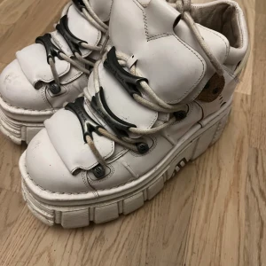 New Rock vita plattform boots - Säljer ett par chunky vita boots från New Rock med rejäl plattformssula och snörning. Skorna har detaljer i beige och svart, robust design och coola metalldetaljer. Tillverkade i skinn med rund tå och högt skaft, perfekta för dig som vill sticka ut.