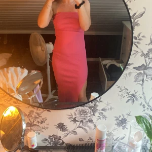 Rosa ribbad axelbandslös långklänning - Säljer en snygg rosa axelbandslös långklänning med ribbad struktur och en slits på sidan. Klänningen har en tight passform och är perfekt för dig som gillar att sticka ut med färg. Enkel och stilren design som ger en cool vibe.