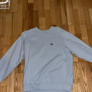 Ljusblå sweatshirt från Yoke, M - Säljer en stilren ljusblå sweatshirt från Yoke i storlek M. Tröjan har en klassisk passform med rund halsringning och diskret logga broderad på bröstet. Tillverkad i mjuk bomull, perfekt för en clean och avslappnad look.