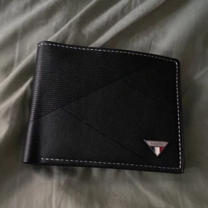 Svart plånbok från Leepiu i skinn - Snygg svart plånbok från Leepiu med coolt geometriskt mönster och kontrasterande vita sömmar. Plånboken är gjord i skinn och har flera fack för kort, mynt och ID-fönster. Perfekt storlek för fickan och stilren design med metallogo